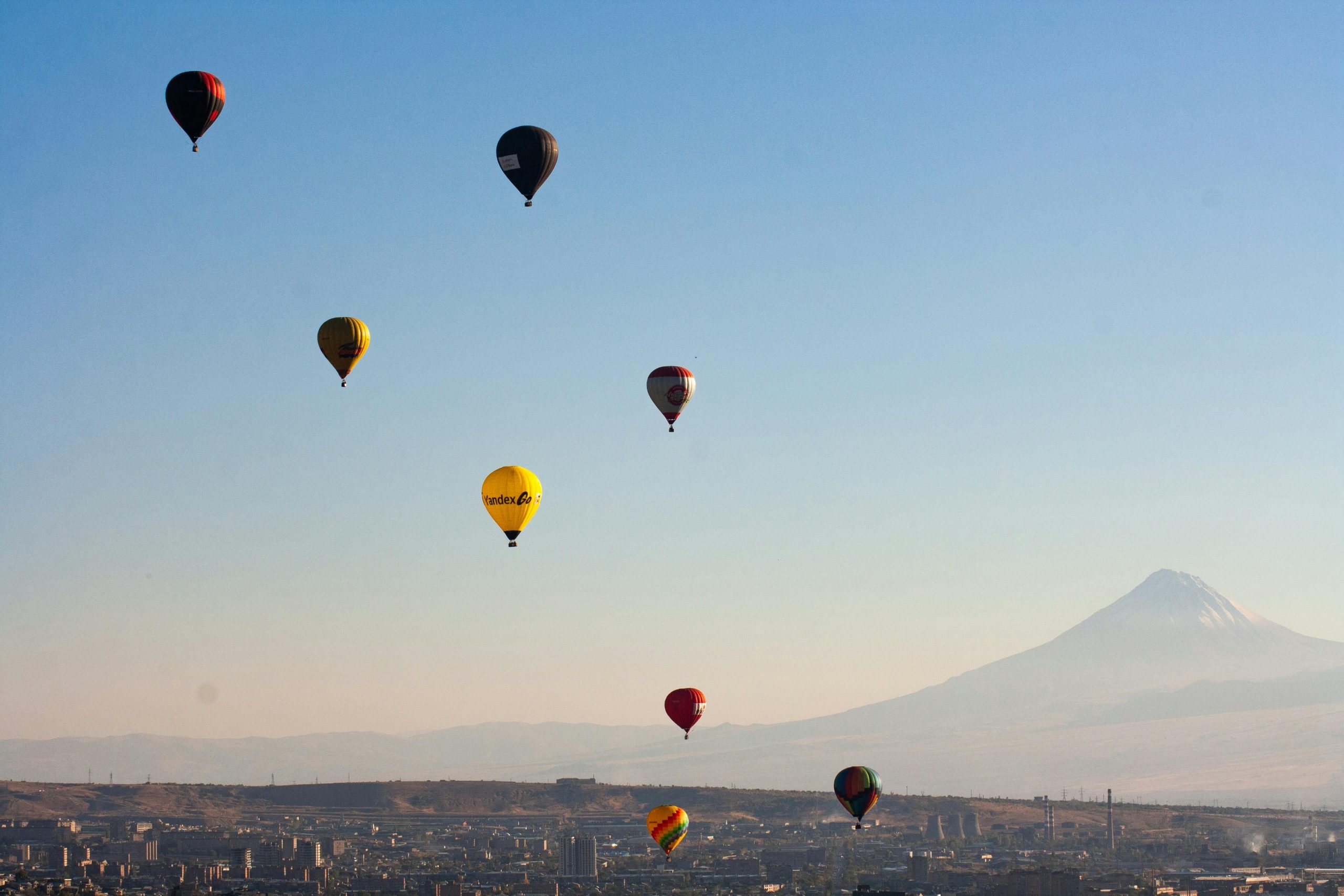 Hot air balloons float over Yerevan with Mount Ararat in the distance during a serene sunrise.